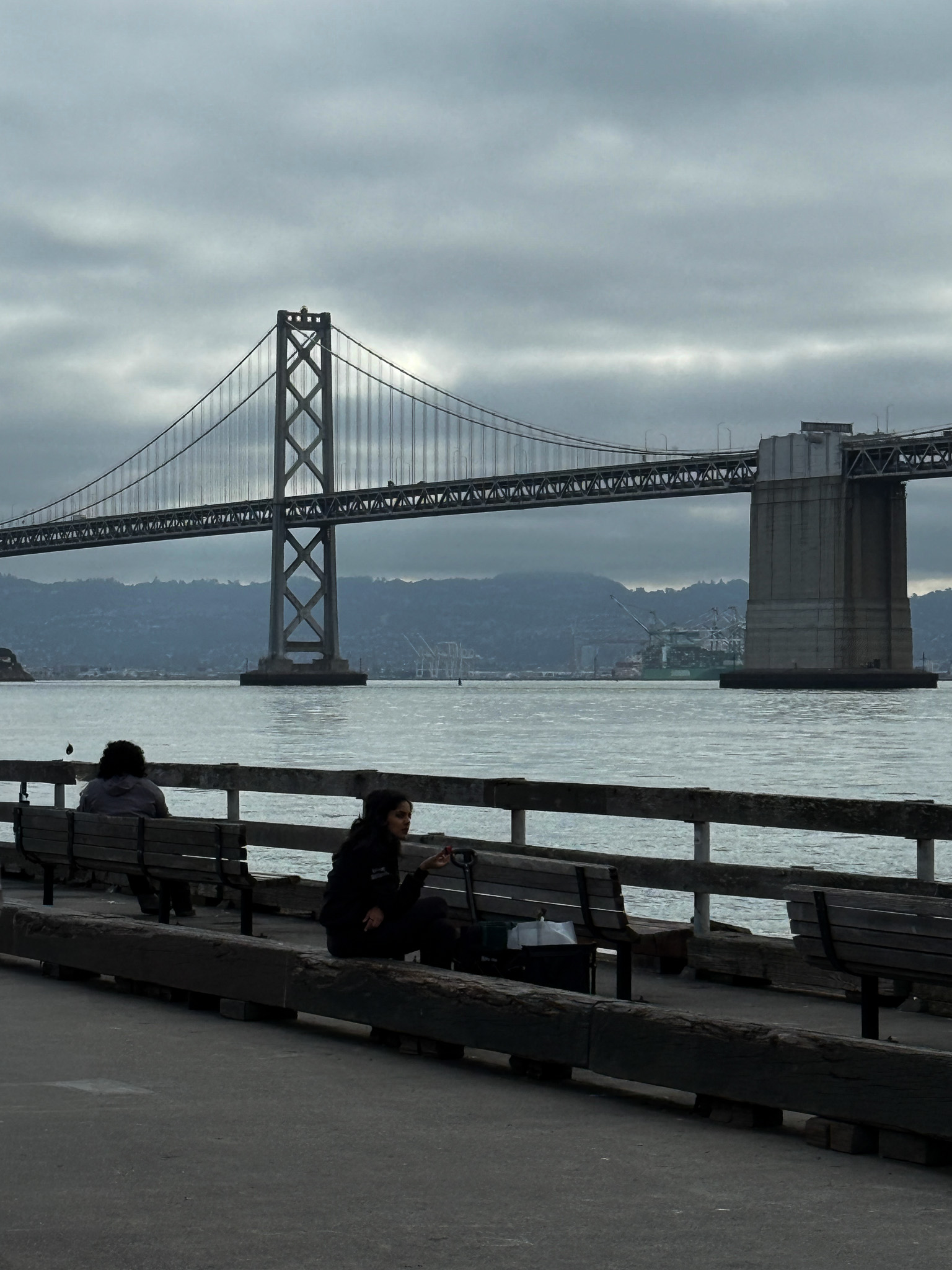 Bay bridge arches with people sitting on benches looking at the Bay and Berkeley hills