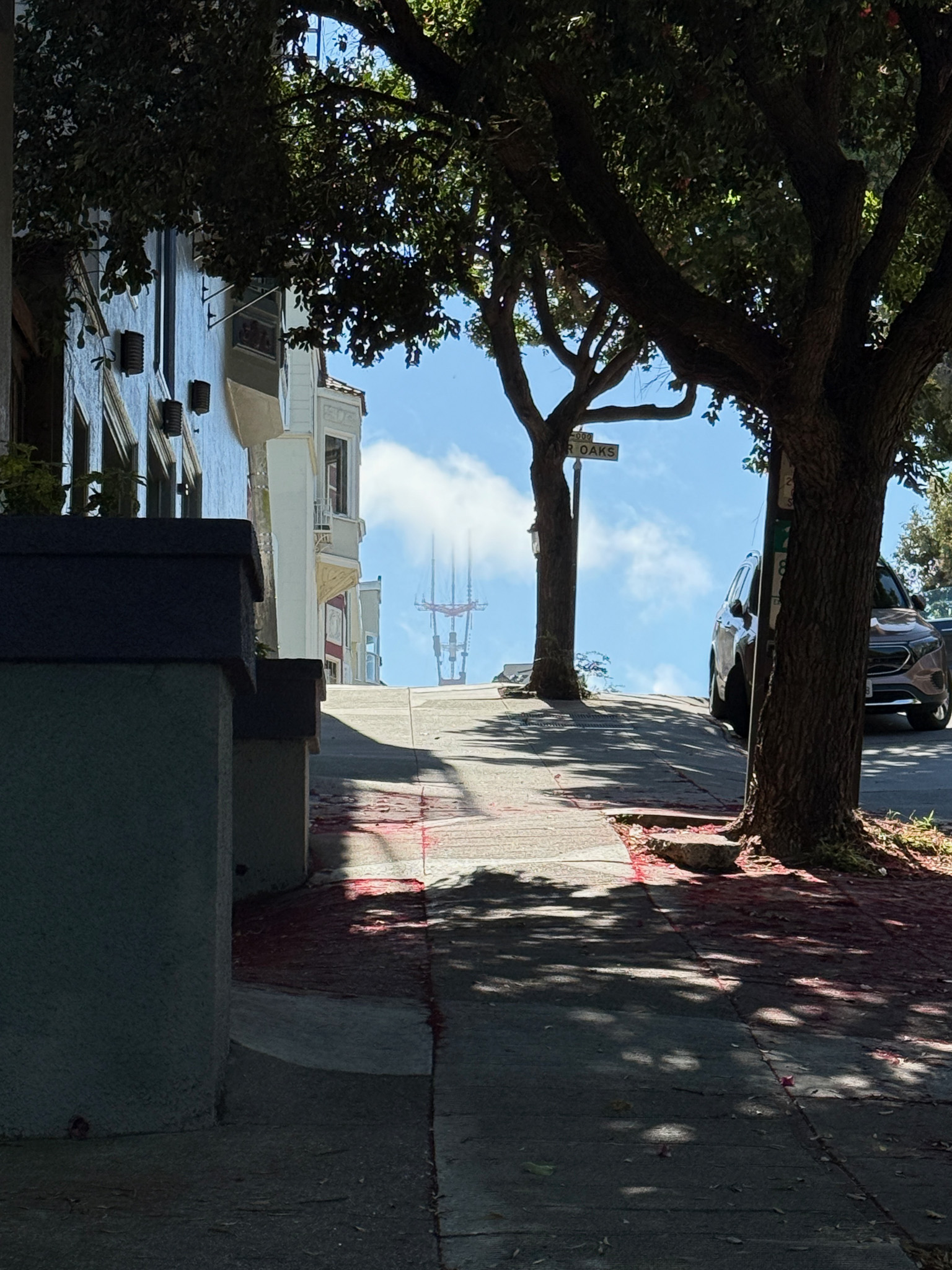 Steep hill and looking over it you see Sutro tower with fog drifting through it.